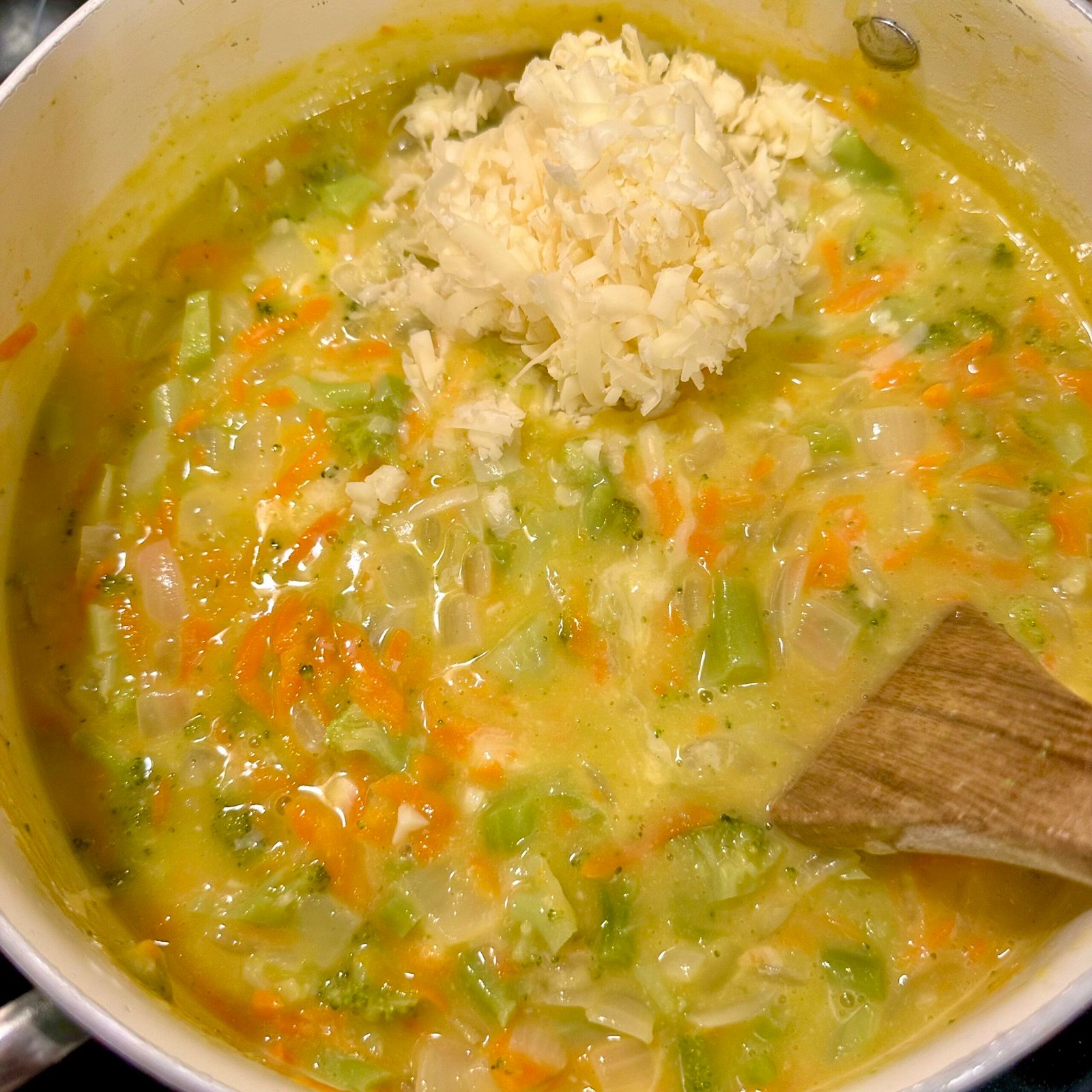 Freshly shredded cheddar cheese being added to a pot of homemade broccoli cheddar soup to melt and thicken the mixture.