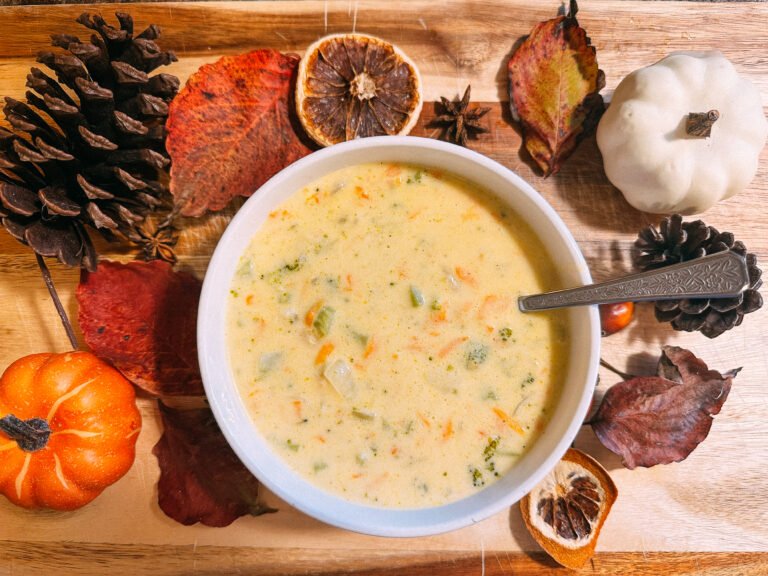 overhead bowl of broccoli cheddar soup surrounded by fall decor and pumpkins