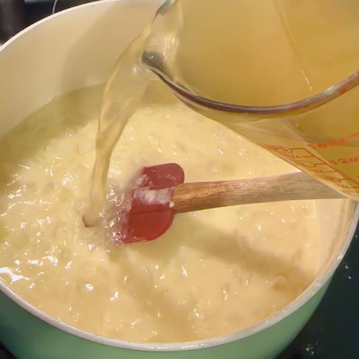 Pouring chicken broth into the onion and flour mixture to create the base for homemade broccoli cheddar soup.